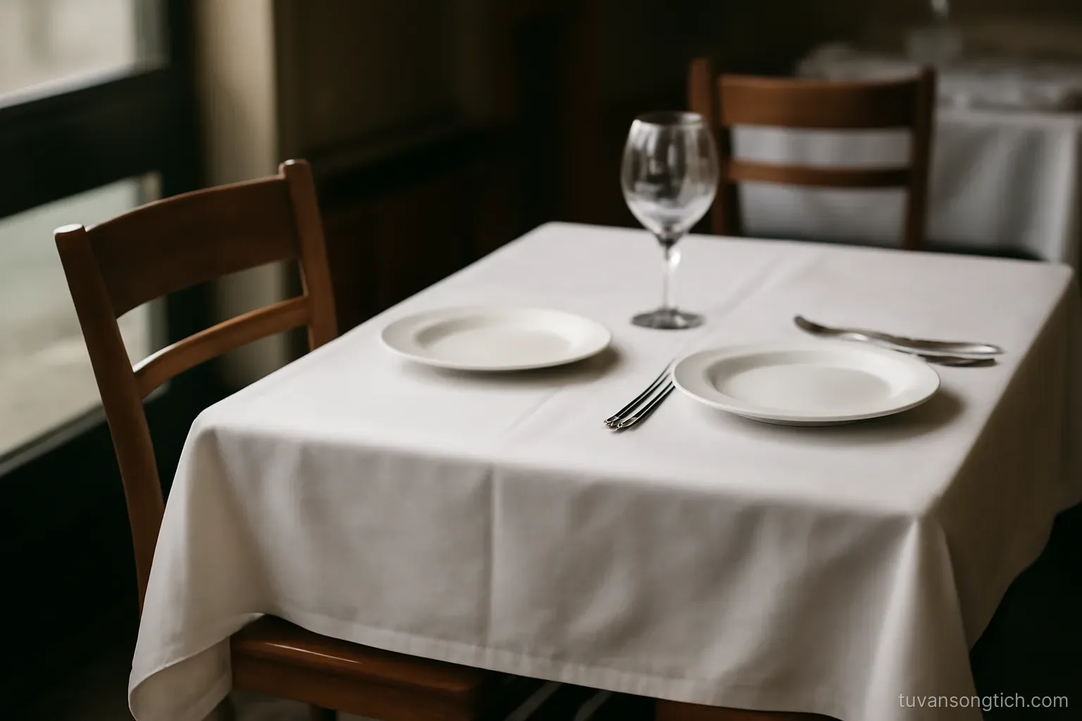 a single chair pushed back from a table set for two, one place setting cleared away
